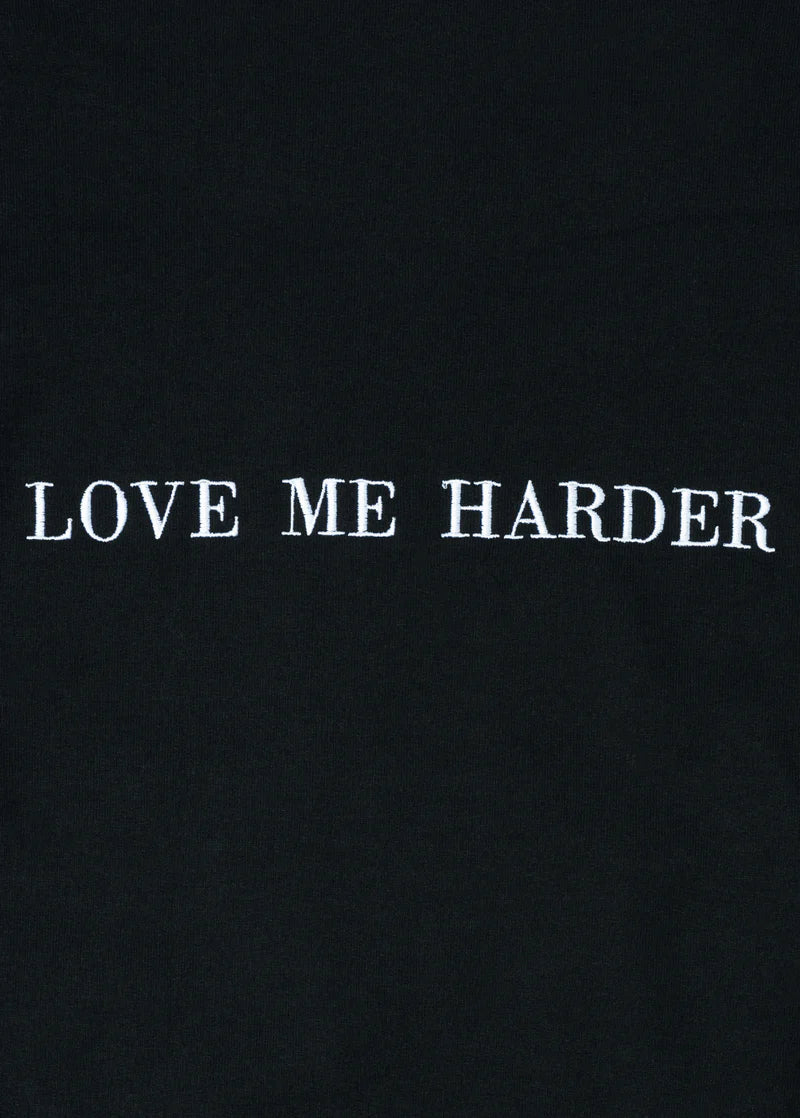 Close-up detail of Ariana Grande Love Me Harder black crewneck featuring clean white embroidered typography graphic