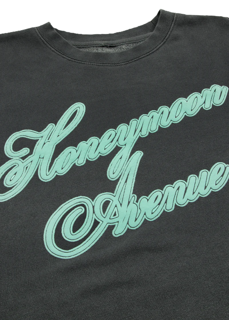Close-up of mint Honeymoon Avenue script graphic on dark charcoal Ariana Grande crewneck