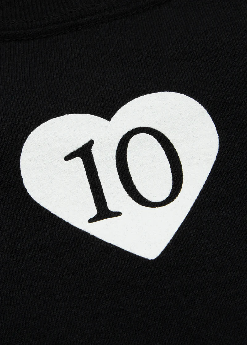 Close-up white heart 10 anniversary graphic on black Ariana Grande merch t-shirt